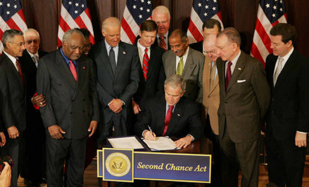 President Bush Signs H.R. 1593, the Second Chance Act of 2007 President Bush seated at desk signs Second Chance Act. Standing Congressional representatives look on. US flags in background