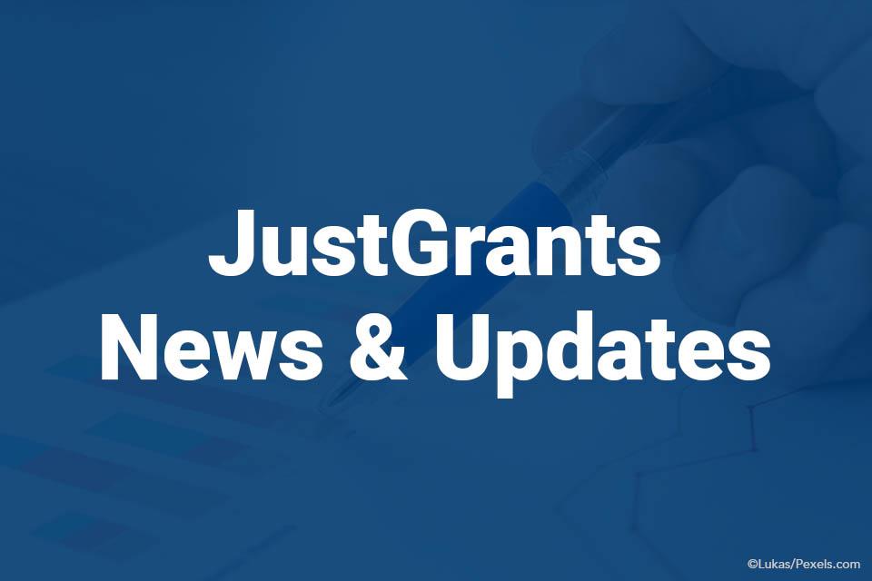 JustGrants News & Updates on blue background with pen in hand